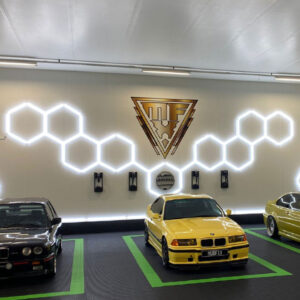 Two yellow bmw cars parked in a garage under Flying Eagle LED Hex Lights.