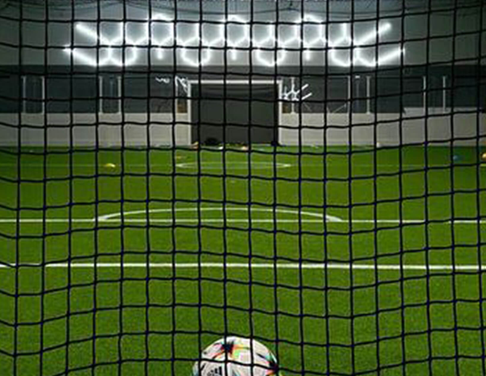 A soccer ball sits in a net under the glow of Hex Lights in a gym.