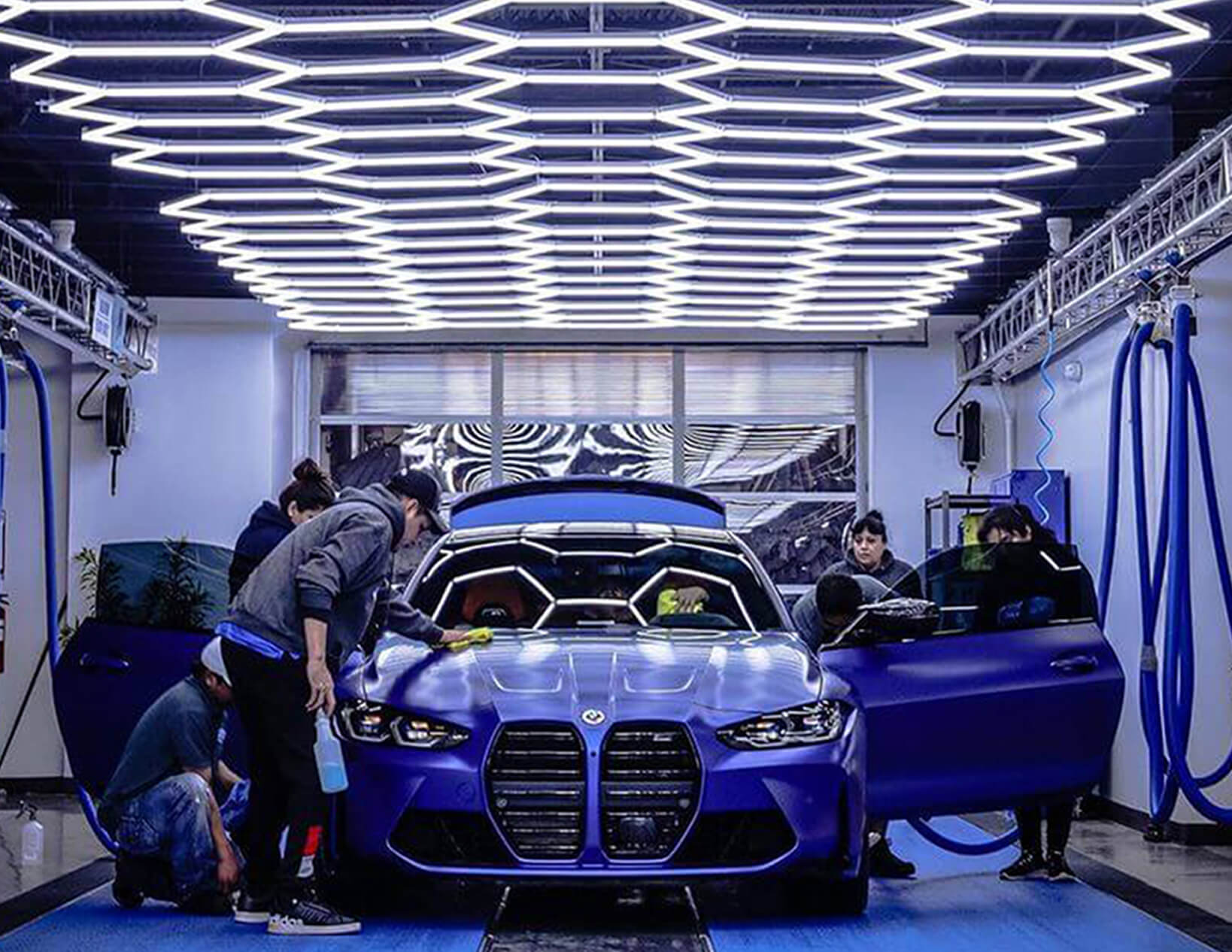 A blue BMW M3 is being washed in a garage under the glow of Canada Hex Lights.