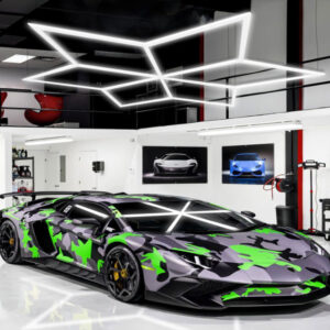 A green and camouflaged Lamborghini with custom White Lotus LED Hex Lights is parked in a garage.